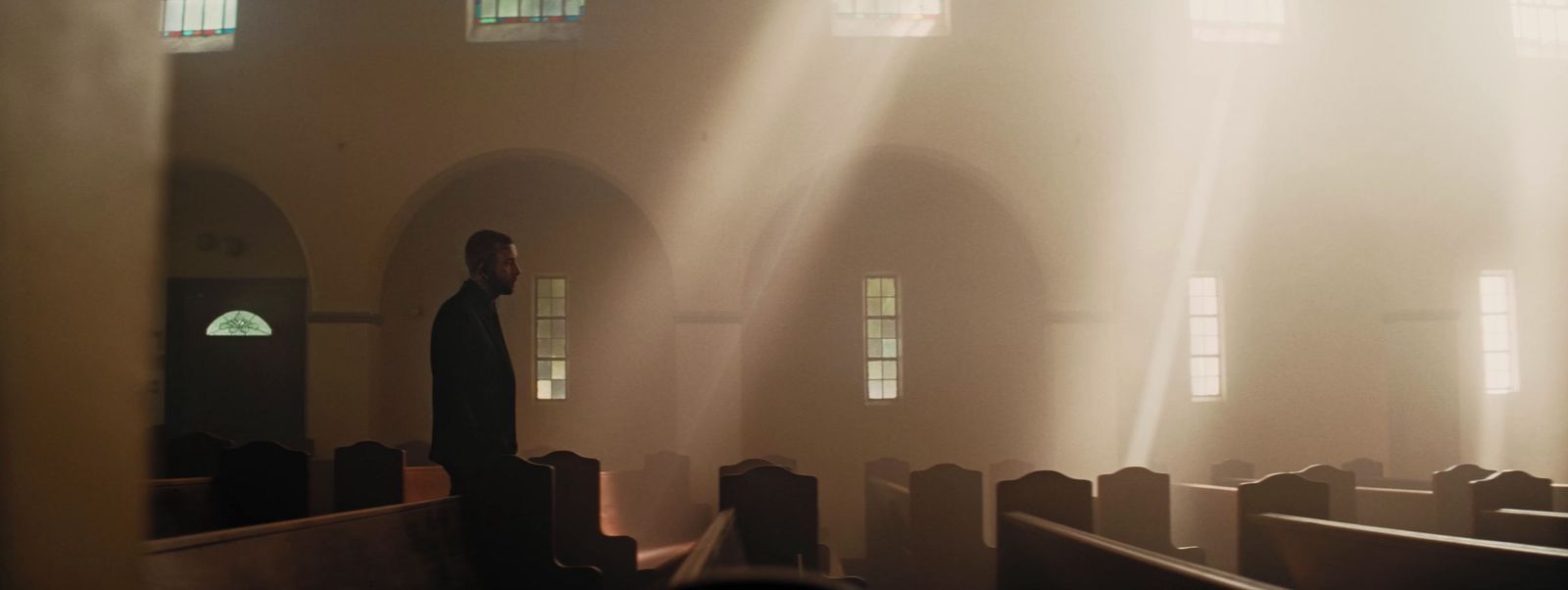 a man standing in a church with sunlight streaming through the windows