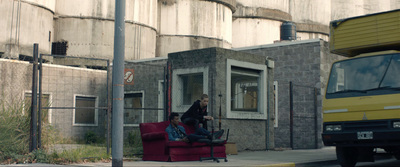 two people sitting on a red chair in front of a building