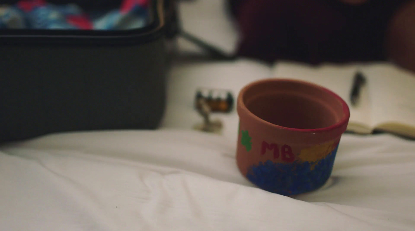 a coffee cup sitting on top of a bed next to an open book