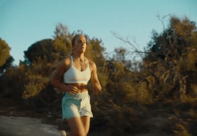 a woman running down a dirt road with trees in the background