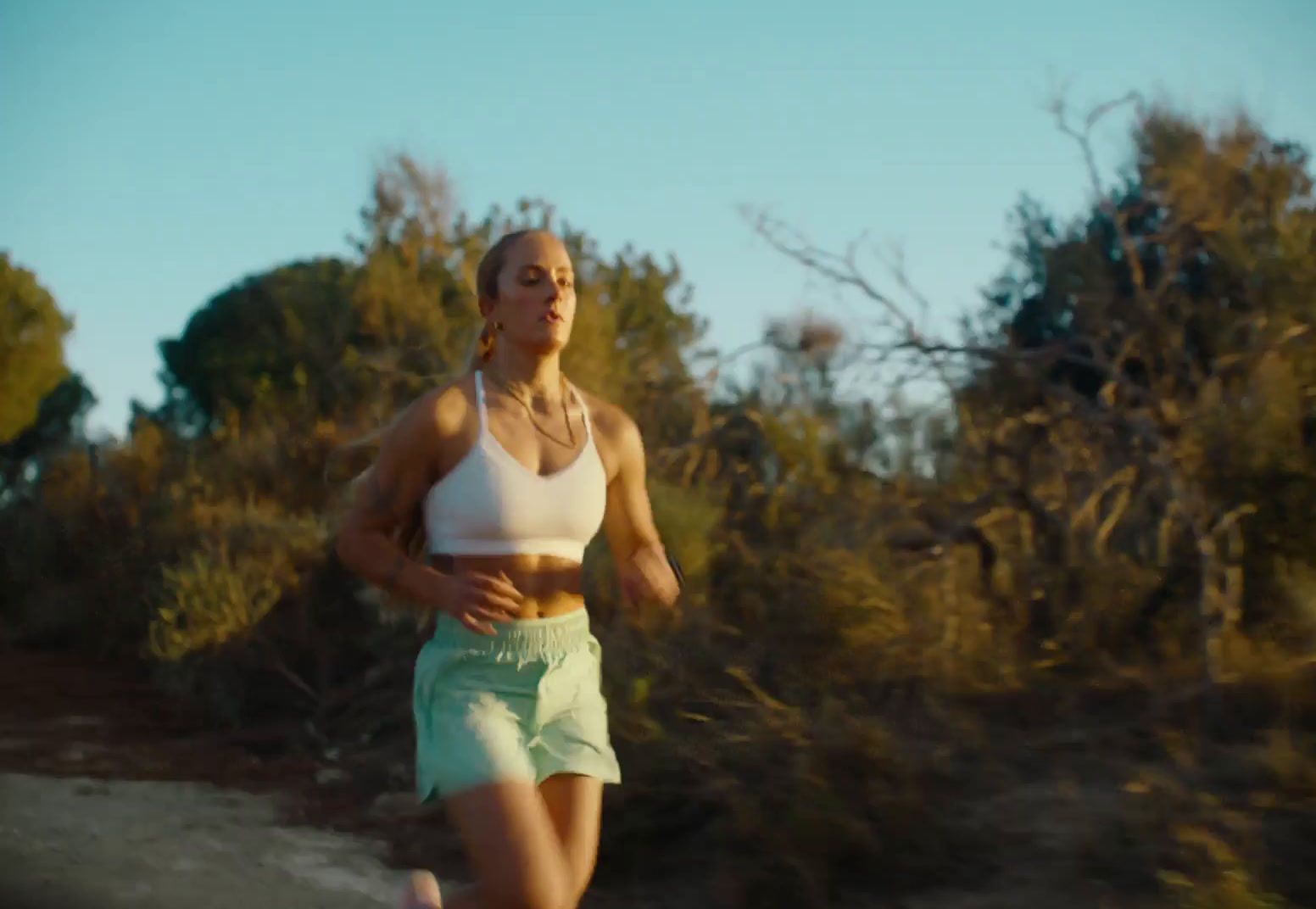 a woman running down a dirt road with trees in the background