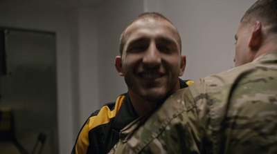 a man in a camo jacket smiles at another man