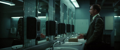 a man in a suit standing in front of mirrors in a bathroom