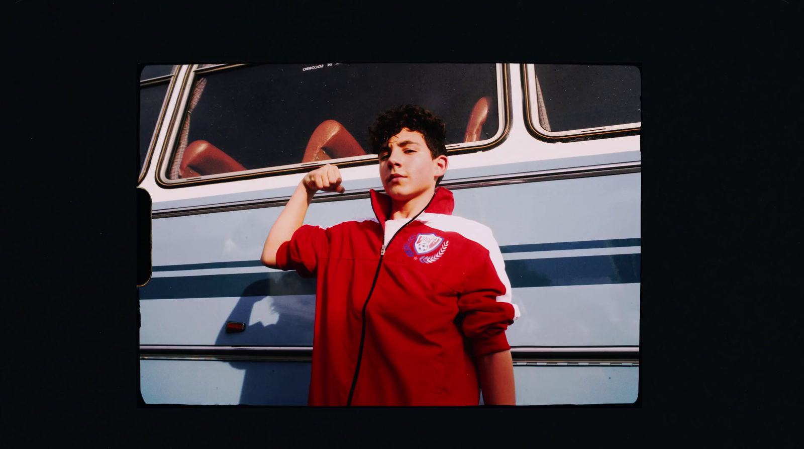 a young man in a red jacket standing next to a bus