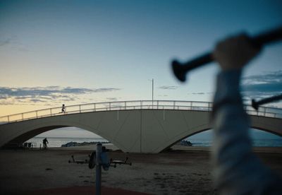 a person holding a baseball bat in front of a bridge