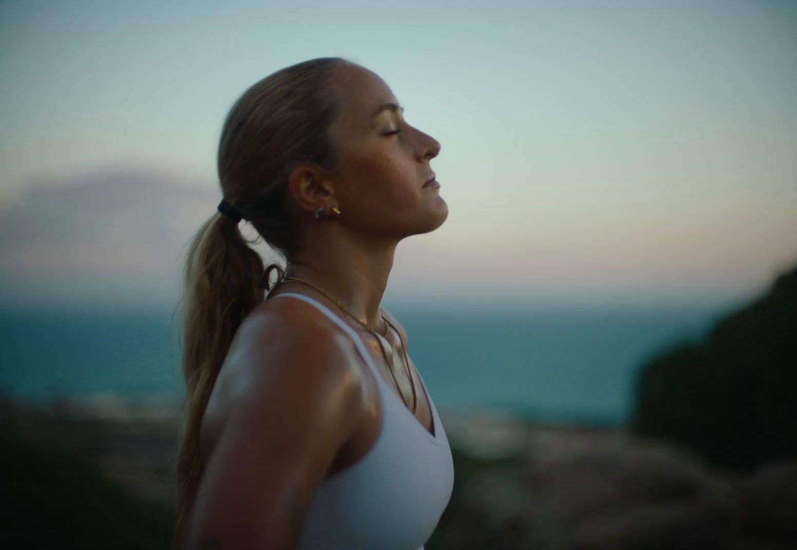 a woman in a white tank top looking up at the sky