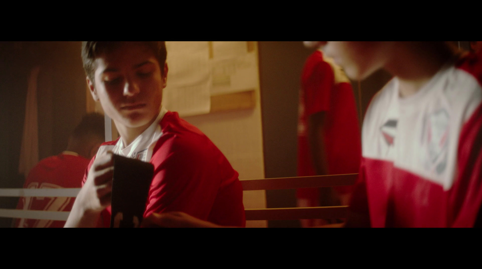 a young man in a red shirt is holding a cell phone