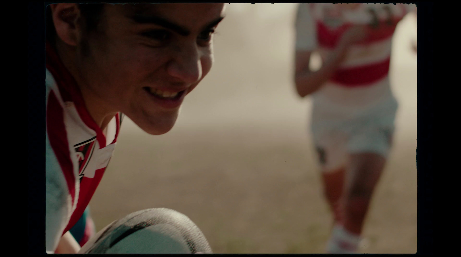 a young man in a red and white striped shirt is holding a rugby ball