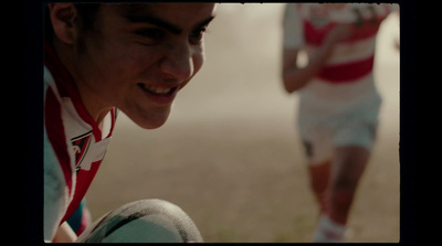 a young man in a red and white striped shirt is holding a rugby ball