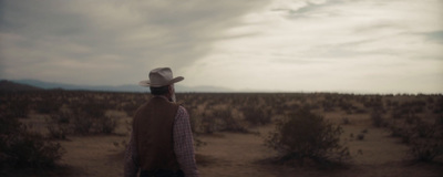 a man in a cowboy hat walking through a desert