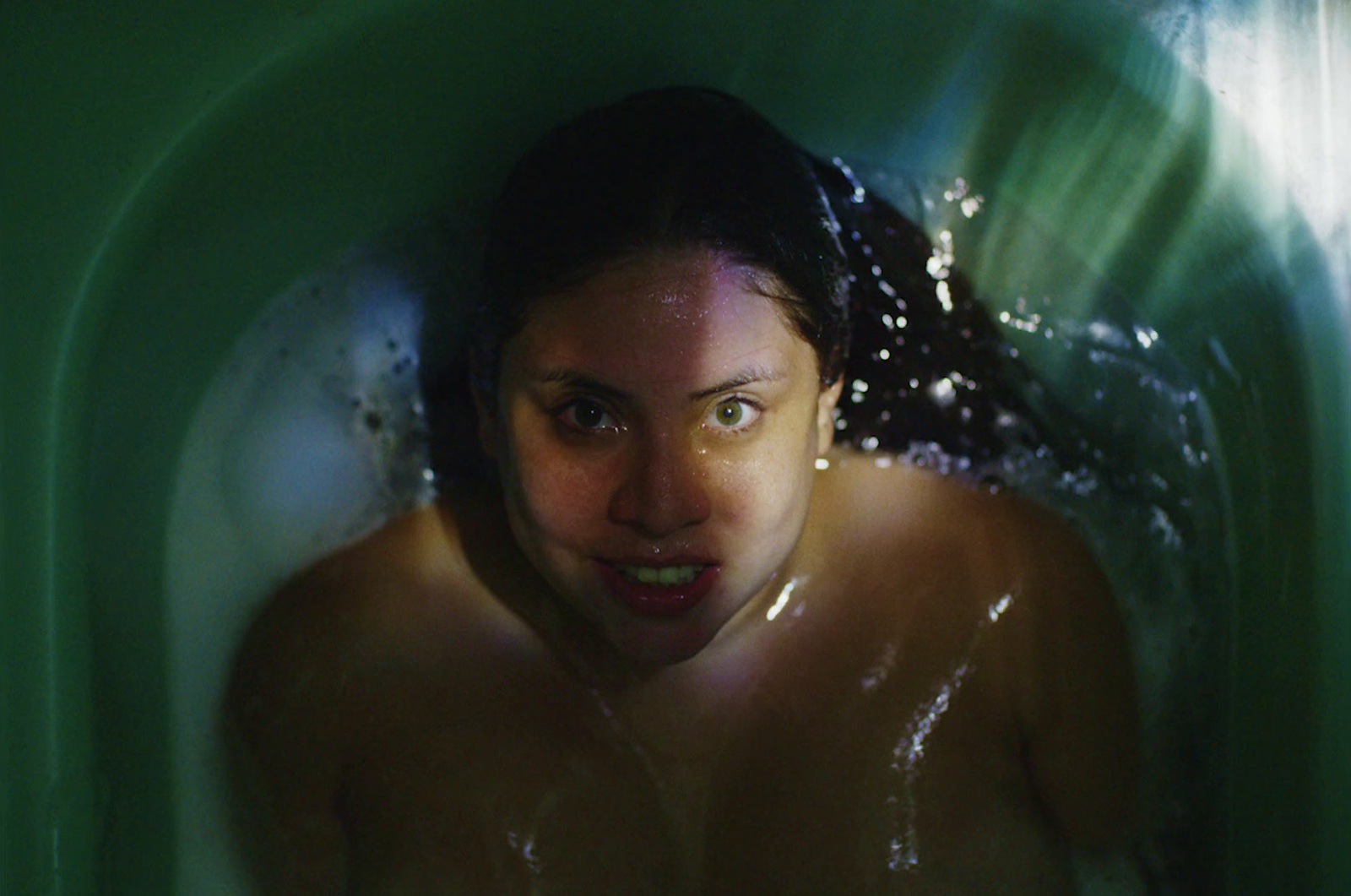 a woman in a green tub with water on her face