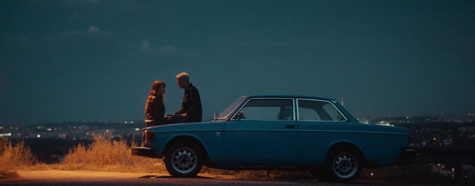 a couple of people sitting on the hood of a car