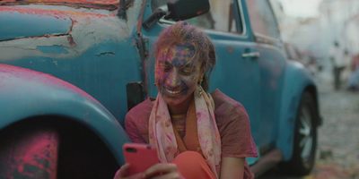 a girl with holi paint on her face is sitting next to a blue car