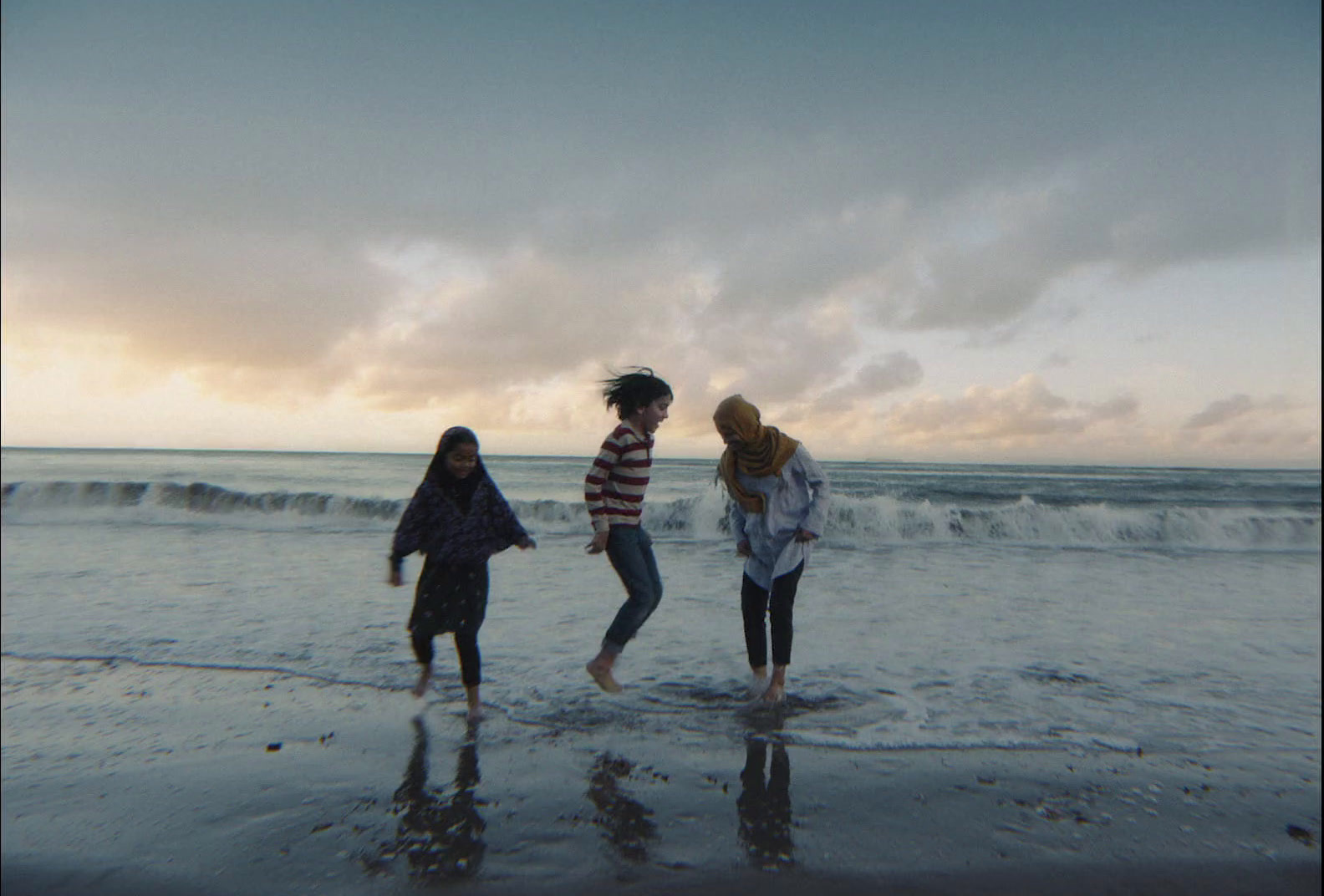 three girls standing on the beach at sunset