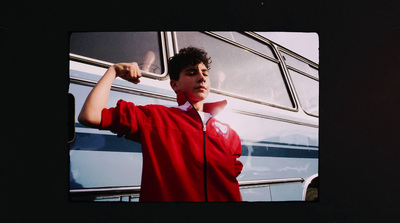 a young man in a red jacket is posing in front of a bus