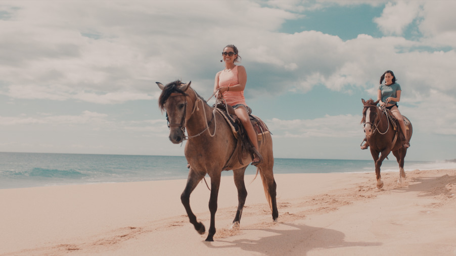 two women riding horses on a beach near the ocean