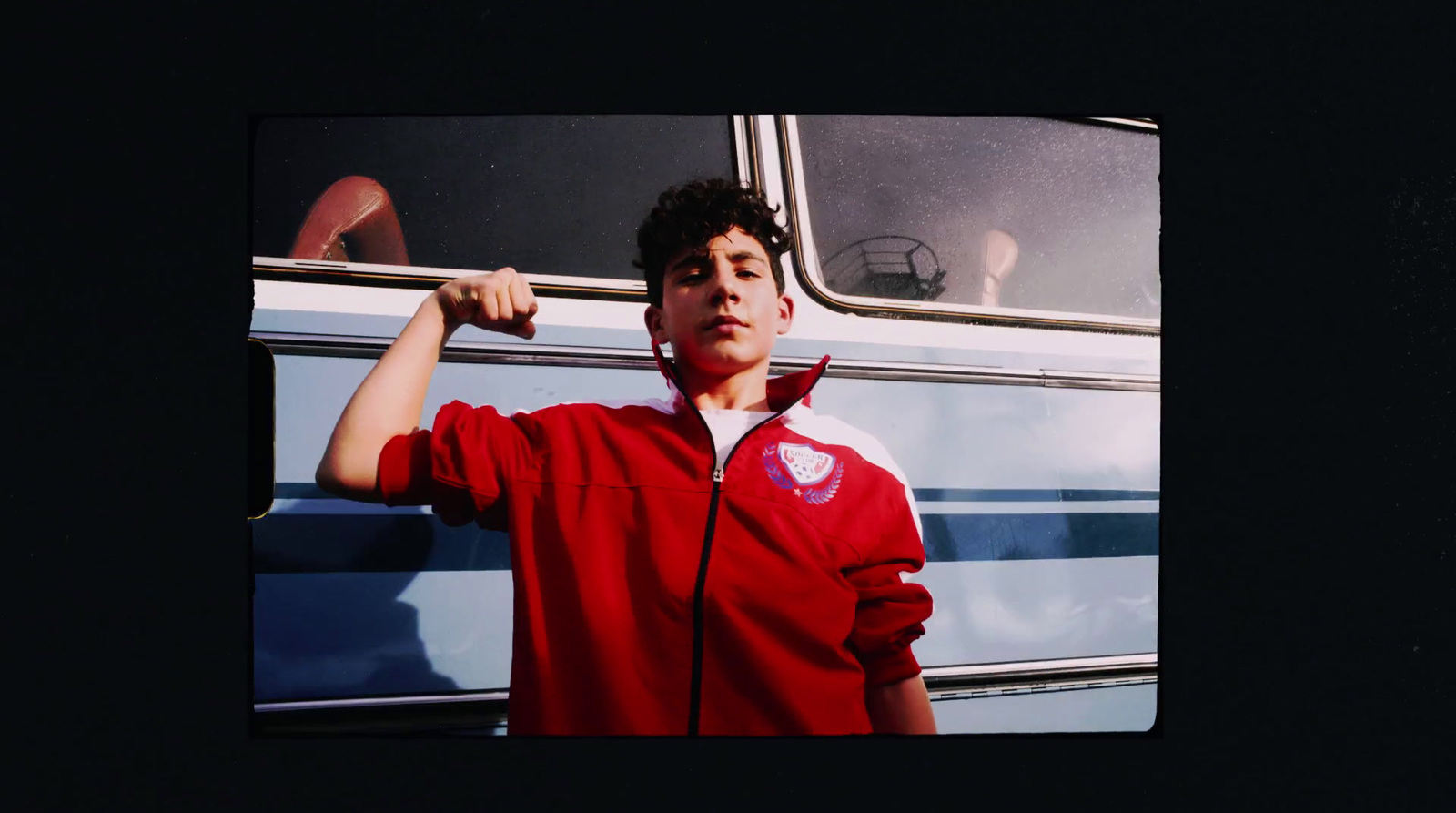 a man in a red jacket is posing in front of a bus