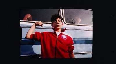 a man in a red jacket is posing in front of a bus