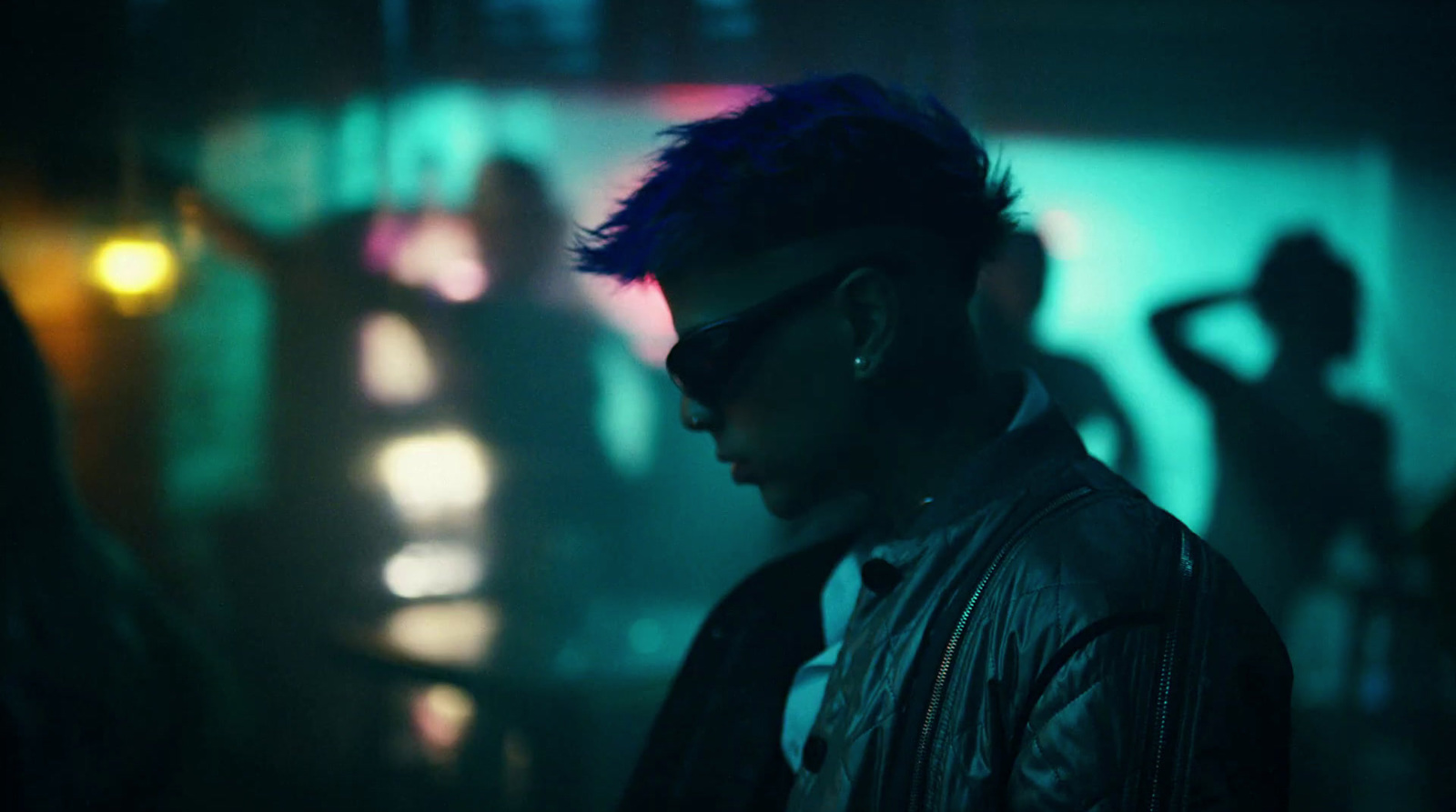 a man in a leather jacket and sunglasses standing in a dark room