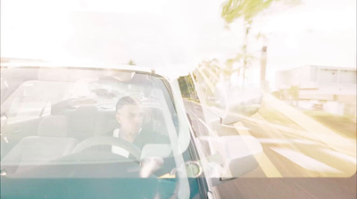 a woman driving a car down a street next to a palm tree