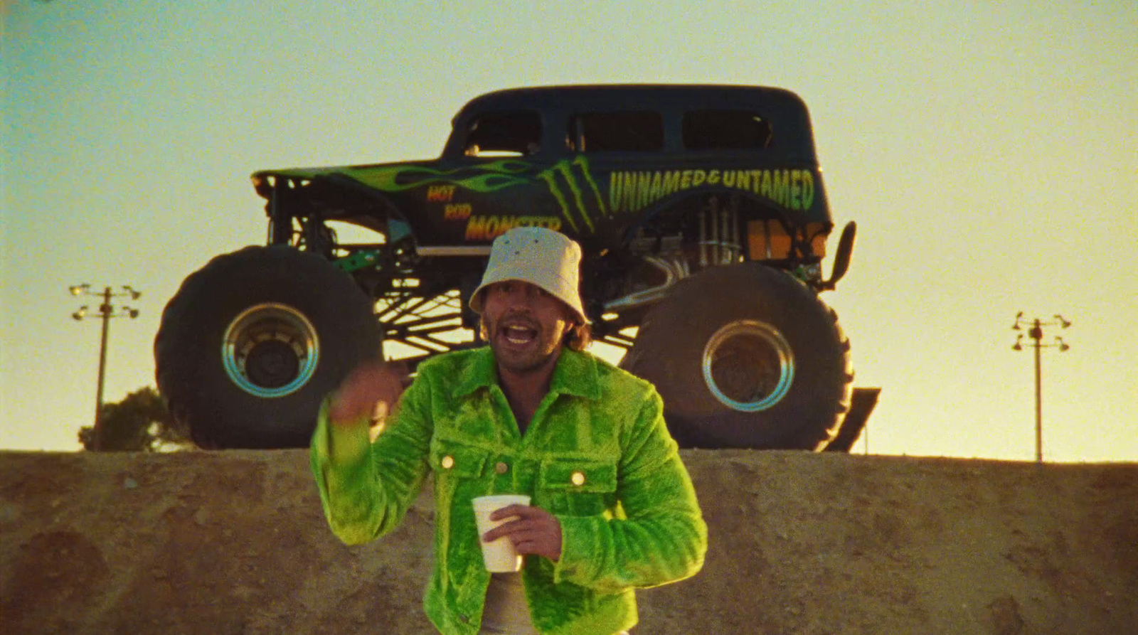 a man in a green jacket standing next to a monster truck