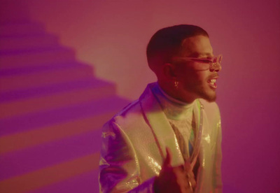 a man in a white jacket and glasses standing in front of a purple background