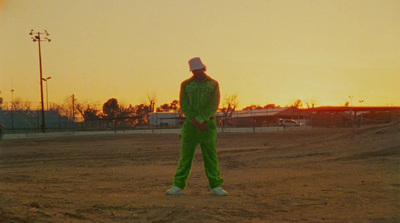 a man in a green outfit standing in a dirt field