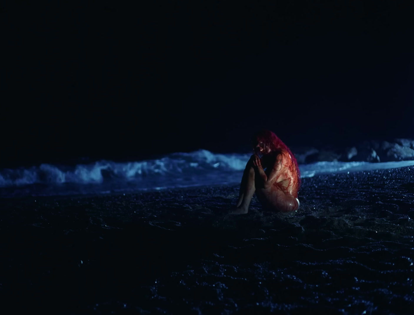 a woman with red hair sitting in the ocean at night