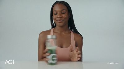 a woman sitting at a table with a jar of liquid