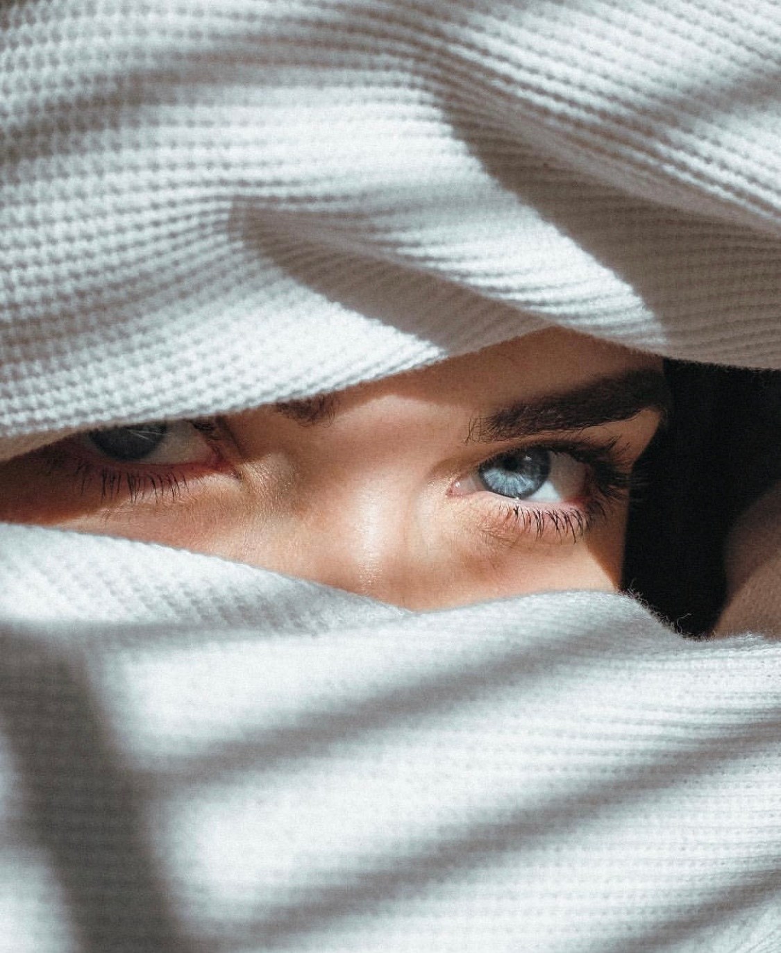 a woman with blue eyes hiding under a blanket