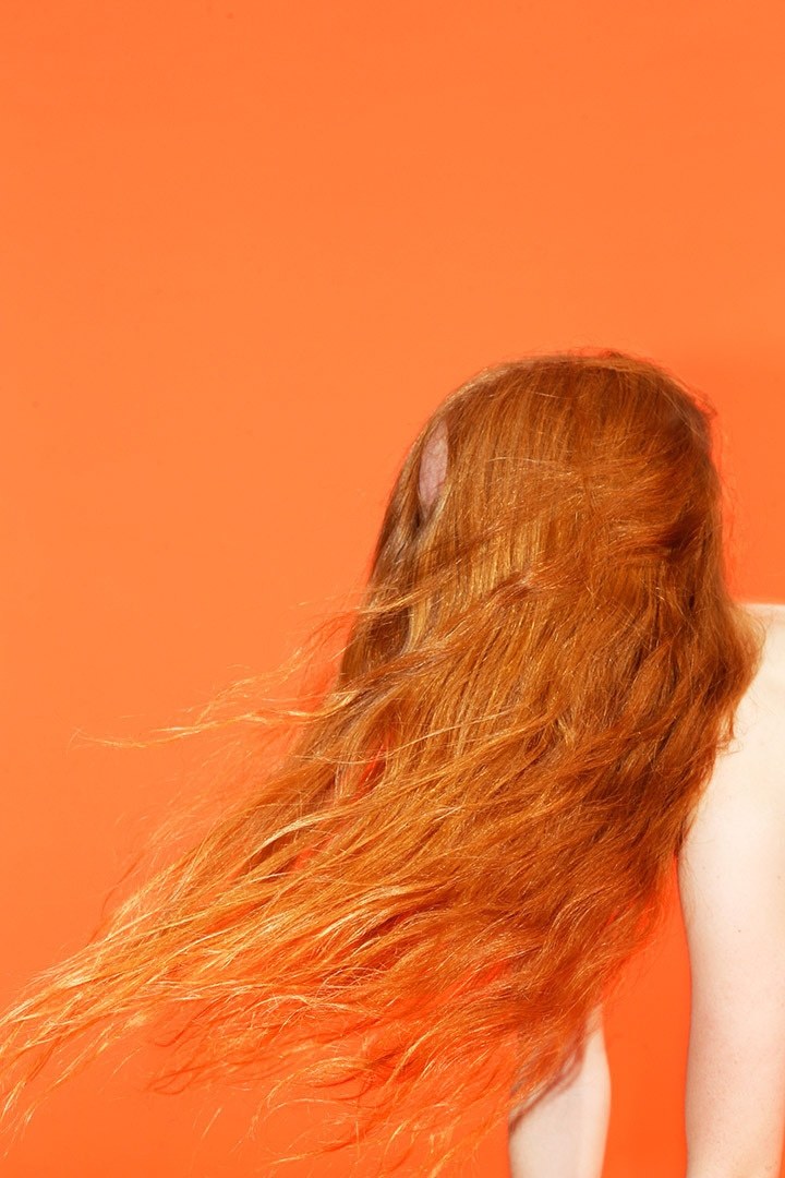 a woman with long red hair standing in front of an orange background