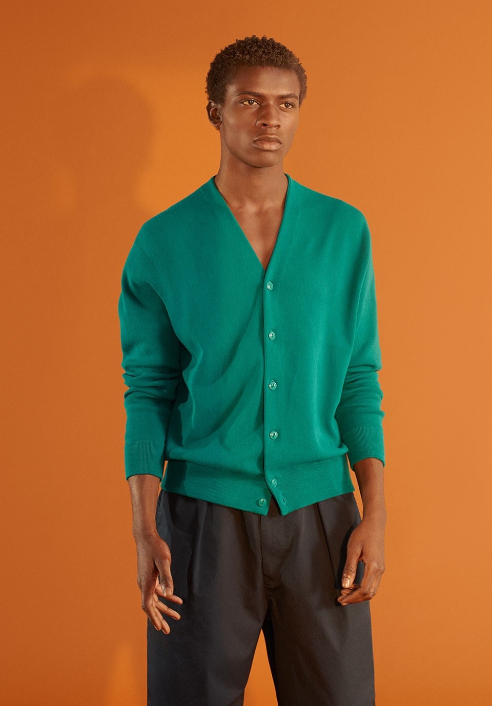 a man in a green cardigan standing in front of an orange wall