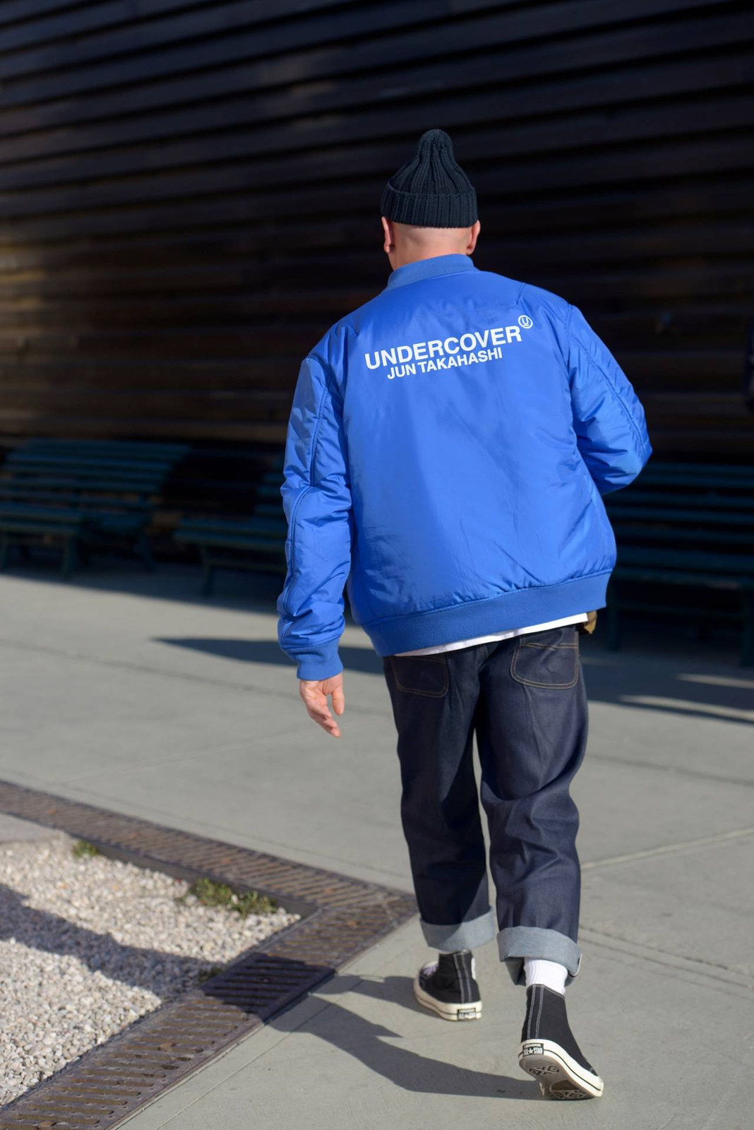 a man walking down a sidewalk wearing a blue jacket