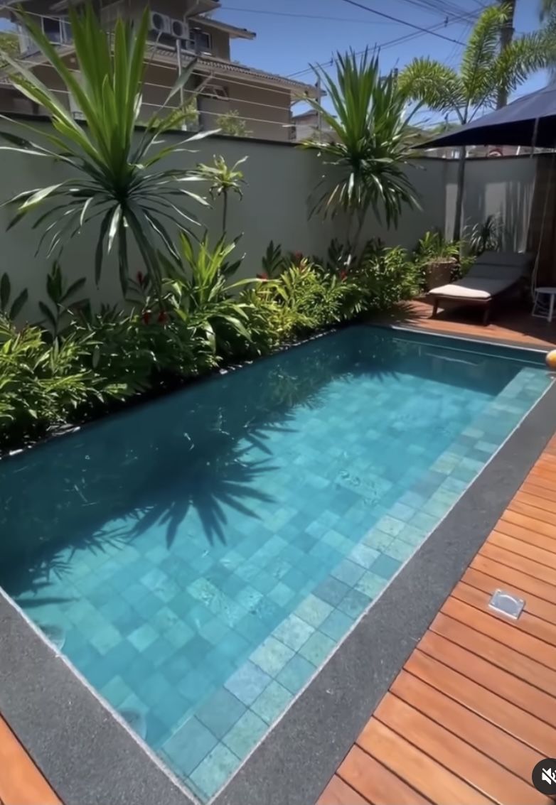 a small swimming pool surrounded by greenery and a wooden deck