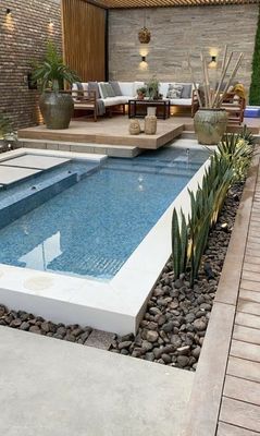 a backyard with a pool surrounded by rocks and plants