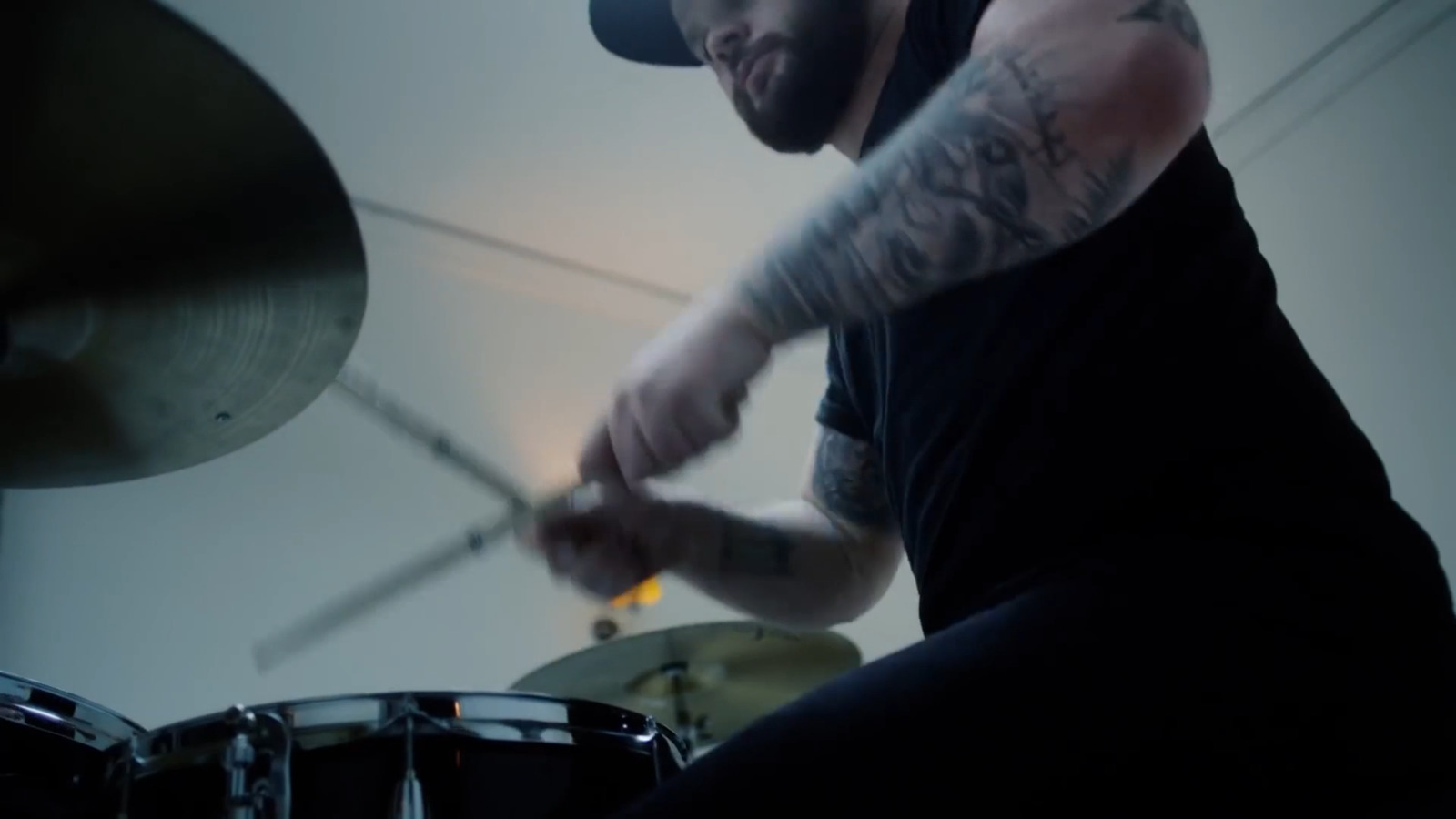 a man with tattoos playing drums in a room