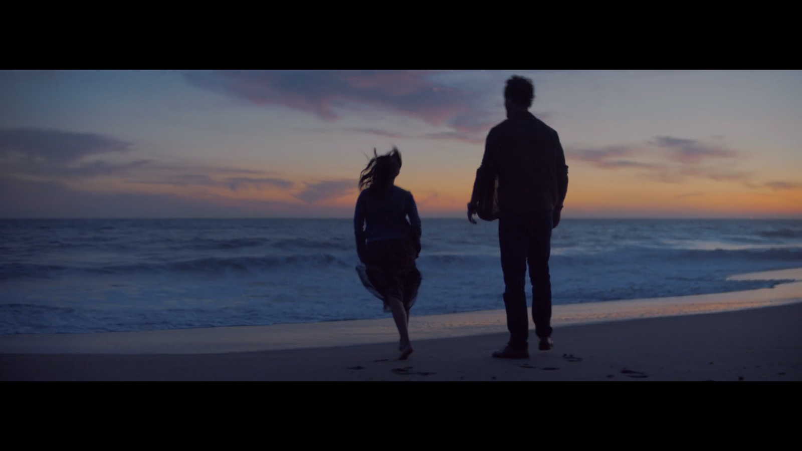 a man and a woman standing on a beach at sunset