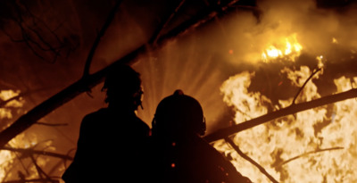 two people standing in front of a fire