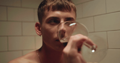 a shirtless man drinking from a wine glass