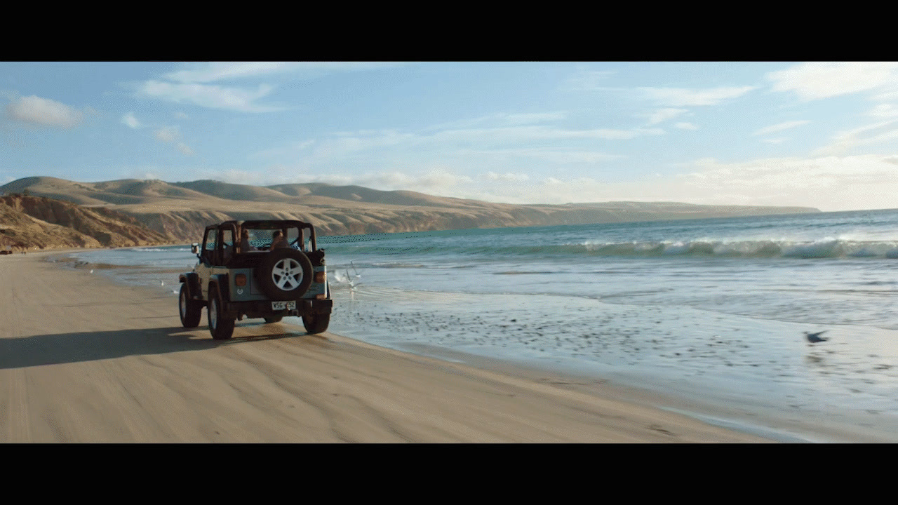 a jeep driving down a beach next to the ocean