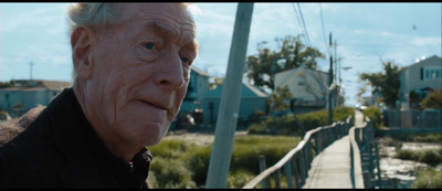 an older man standing on a boardwalk in front of houses