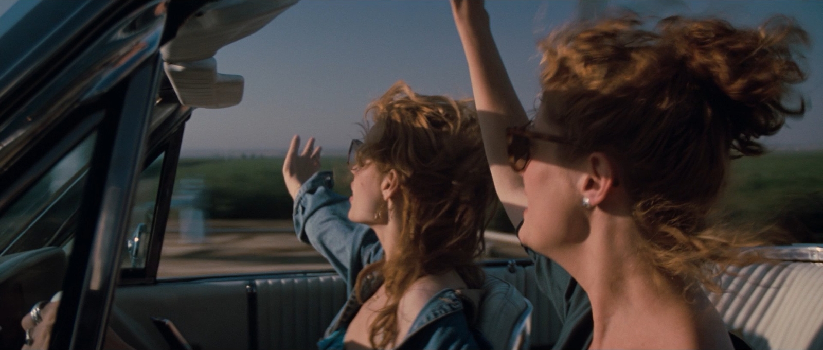 two women sitting in a car with their hands in the air