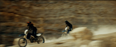 a couple of people riding motorcycles down a dirt road