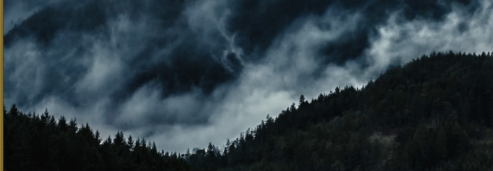 a mountain covered in clouds and trees under a cloudy sky