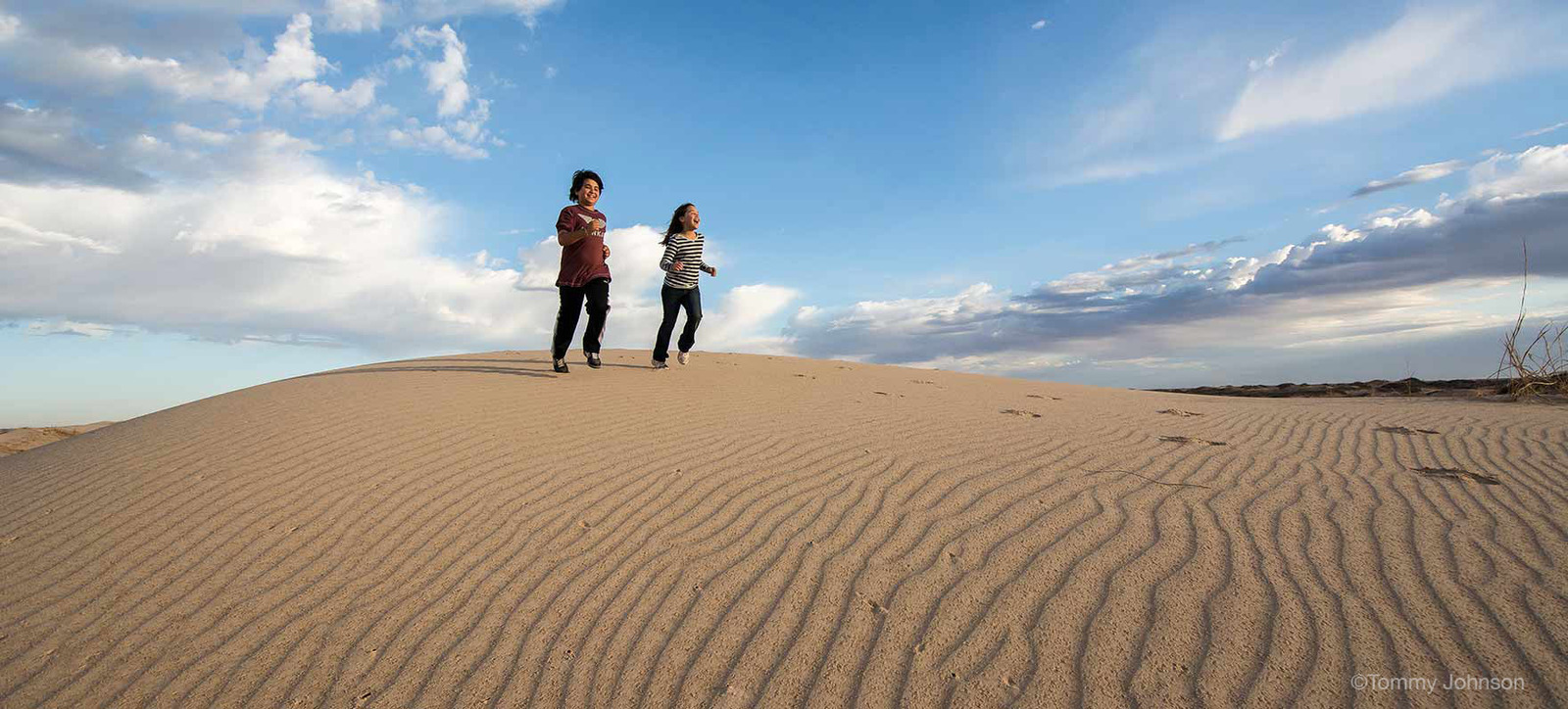 two women standing on top of a sand dune