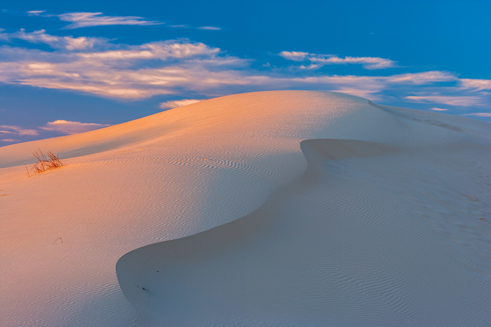 a large sand dune under a cloudy blue sky