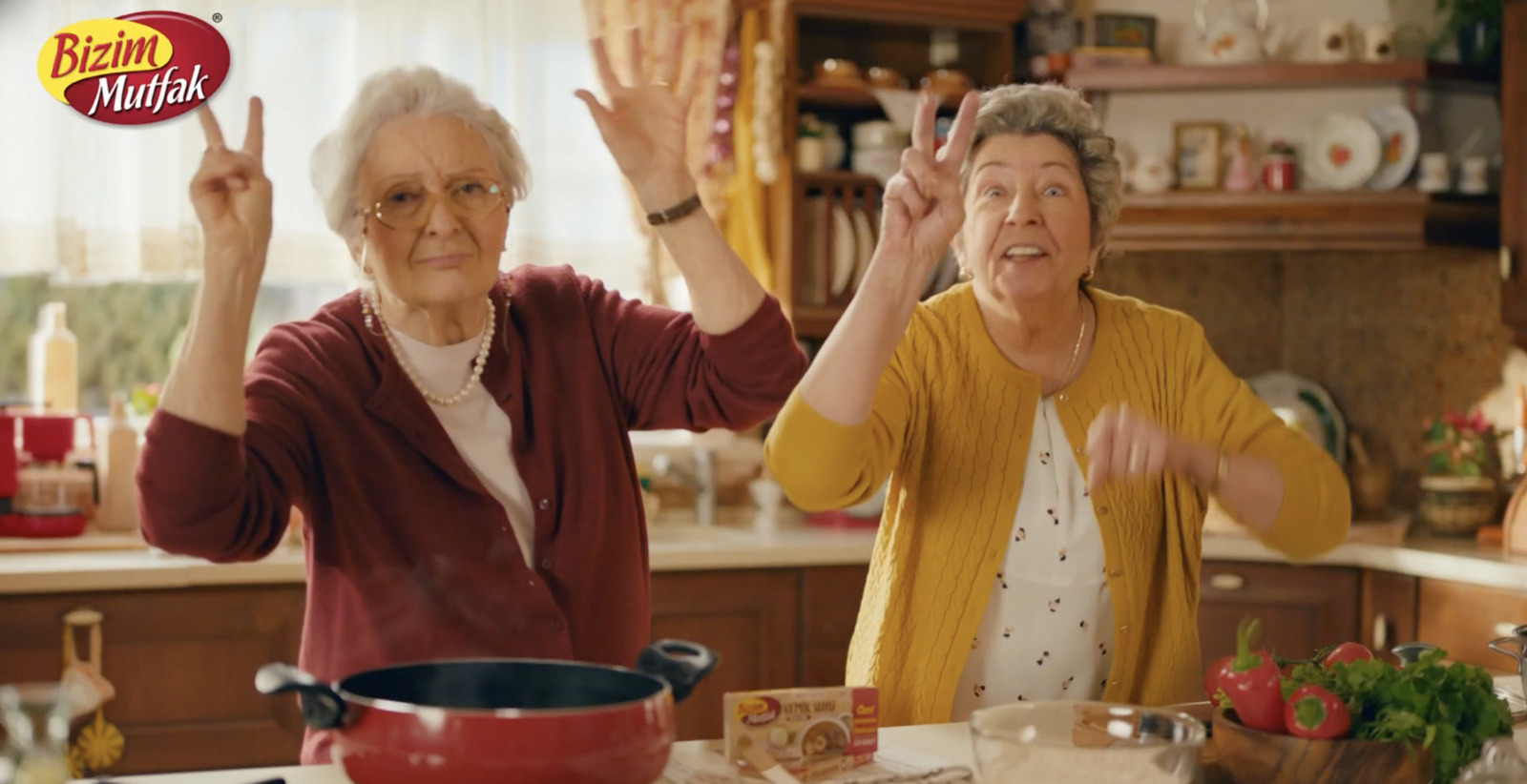 two older women in a kitchen with one holding her hands up