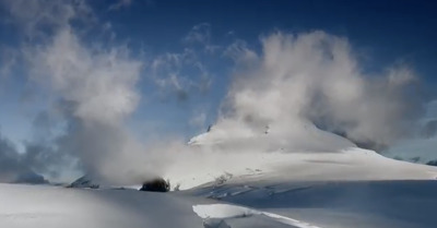 a mountain covered in snow under a cloudy blue sky