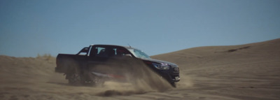 a black truck driving through a sandy field