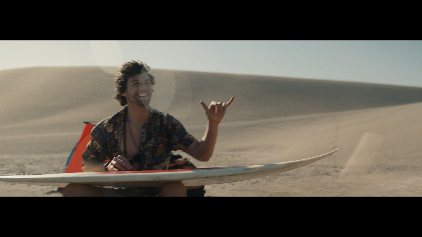 a man sitting on top of a surfboard in the sand